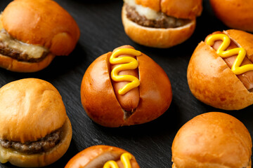 Mini hamburgers, burger and hot dogs with yellow mustard on black slate board