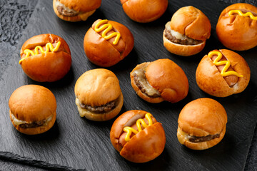 Mini hamburgers, burger and hot dogs with yellow mustard on black slate board