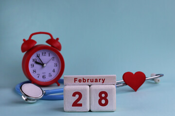 February 28st. White wooden calendar blocks with date, clock and stethoscope on blue pastel...