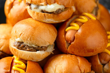 Mini hamburgers, burger and hot dogs with yellow mustard on black slate board