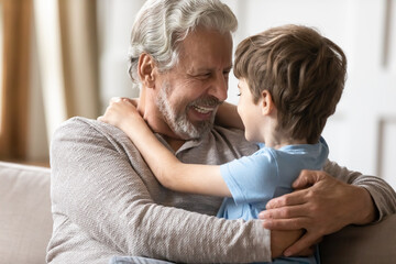 Close up loving grandfather and little grandson enjoying tender moment, sitting on couch at home,...