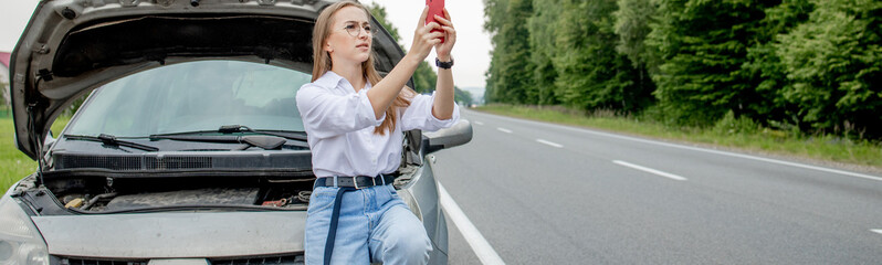 Young woman standing near broken down car with popped up hood having trouble with her vehicle....