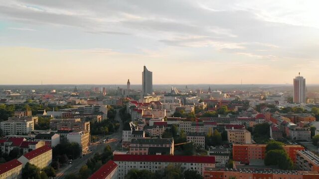 Aerial view over buildings in Leipzig city, the City-Hochhaus in the background, during sunset, in Saxony, Germany - pull back, drone shot