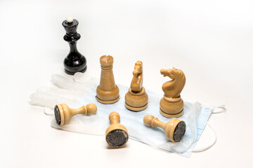 wooden chess pieces on a medical mask. Black's Queen is watching from afar