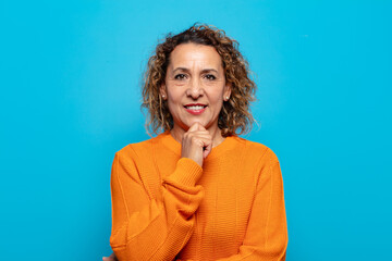 middle age woman looking happy and smiling with hand on chin, wondering or asking a question,...
