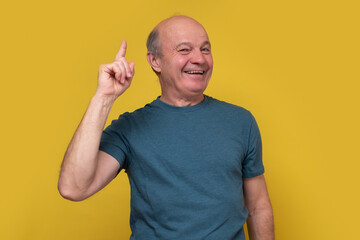 Senior hispanic man pointing one index finger up. Studio shot on yellow wall.