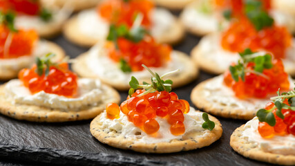 Salmon caviar and soft cheese savory crackers with sesame and poppy seeds served on black slate board