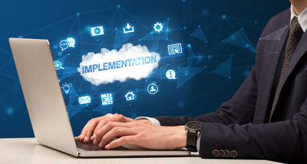 Businessman working on laptop with IMPLEMENTATION inscription, modern technology concept