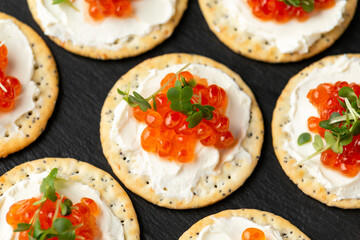 Salmon caviar and soft cheese savory crackers with sesame and poppy seeds served on black slate...