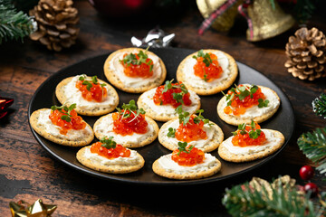 Salmon caviar and soft cheese savory crackers with decoration, gifts, green tree branch on wooden rustic table.