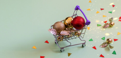 Glittering Christmas baubles and  balls in mini shopping carriage on the paper background.