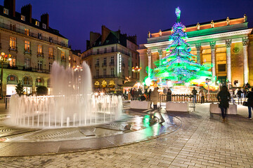 Festivités de Noël sur la place d'une ville en hiver, avec jets d'eau et manège en forme de...