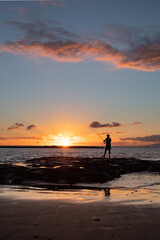 Fototapeta na wymiar Silhouette of man fishing on the sea coast at sunset