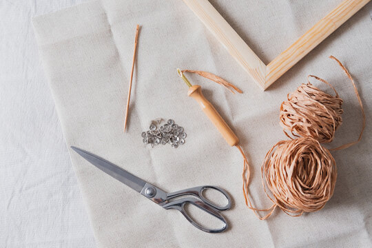 Knitting, handmade, handicraft hobby objects shot from above. Wood frame, macrame threads, needles and scissors in natural linen backdrop