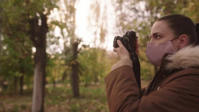 Beautiful Girl Wearing Face Mask Taking Pictures In The Park Using DSLR Camera In Autumn. - close up shot, slowmo