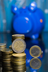 Euro coins with a lot of stacked coins and piggy bank in the background.