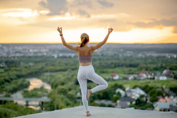 Yoga and meditation with big city on background. Young woman doing yoga on the roof