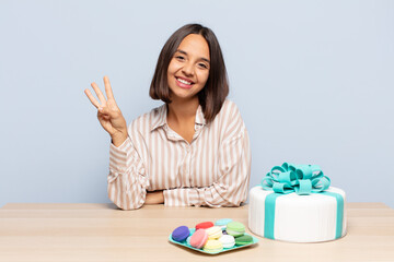 hispanic woman smiling and looking friendly, showing number three or third with hand forward,...