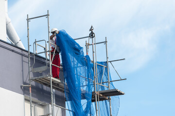Fototapeta premium obrero sobre un andamio de obra extendiendo una red de seguridad sobre la fachada
