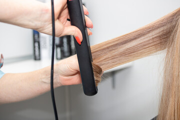 Barber straightens long hair with a hair iron, close-up.