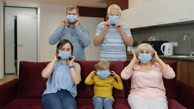 Coronavirus Quarantine Lockdown Concept. Mother, Father, Daughter, Senior Grandparents Puts Medical Masks On Faces At Home. Multigenerational Family Wearing Protective Masks. Life In Covid-19 Pandemic