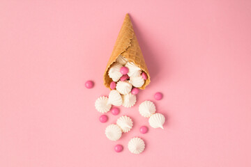 Top view of ice cream cone with white meringue and candy on the pink background