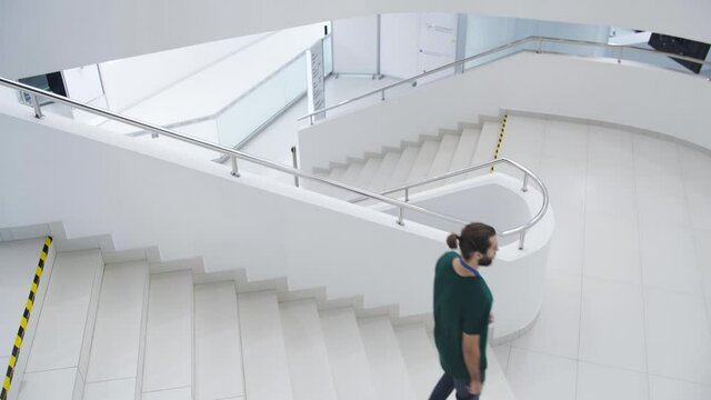 Men with badges in white building. Media. Young men with badges walk up white stairs. Young employees with badges walk in white building