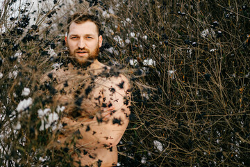 Portrait of ginger brutal naked man with beard posing among bushes
