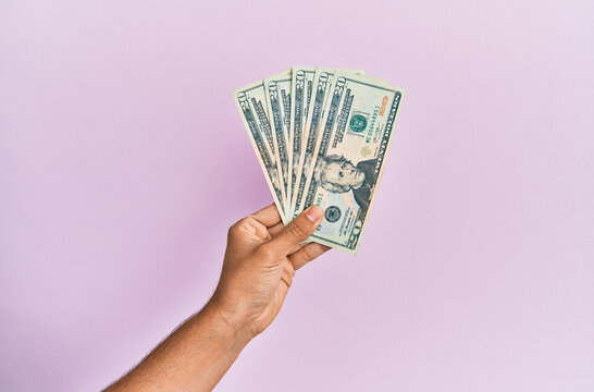 Hispanic hand holding 20 usa dollars banknotes over isolated pink background.