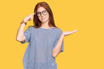 Young read head woman wearing casual clothes and glasses confused and annoyed with open palm showing copy space and pointing finger to forehead. think about it.