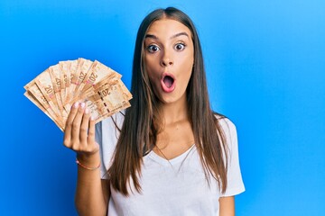 Young hispanic woman holding south african rands banknotes scared and amazed with open mouth for surprise, disbelief face