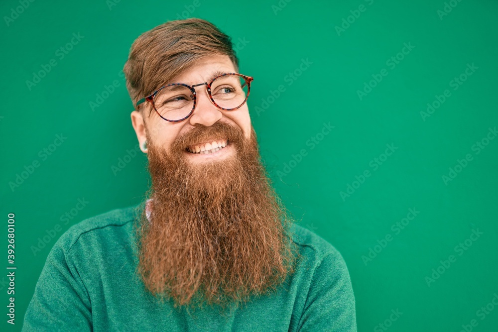 Poster young irish man with redhead beard smiling happy leaning on the wall at the city.