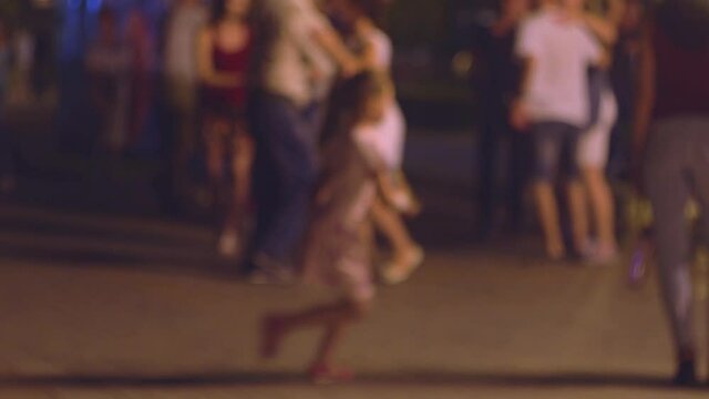 Crowd of couples are dancing social dances in the street and there is little funny girl on foreground trying to imitate, defocused real-time shot.
