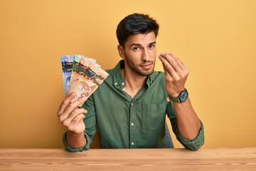 Young handsome man holding canadian dollars doing italian gesture with hand and fingers confident...