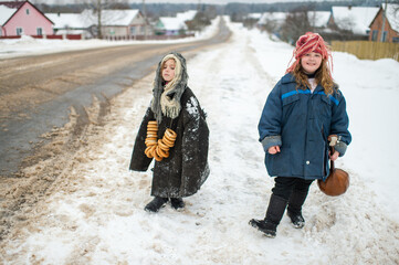 Two beautiful village girls stand on the road with balalaika and barankas in winter
