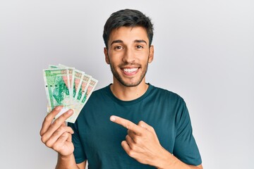 Young handsome man holding 50 hong kong dollars banknotes smiling happy pointing with hand and finger