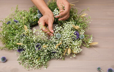 Woman making beautiful wreath of wildflowers at wooden table, closeup