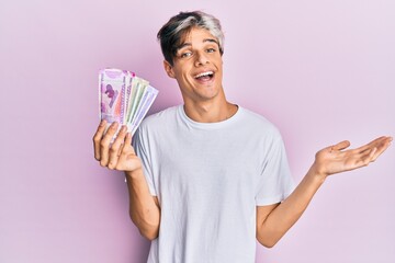 Young hispanic man holding indian rupee banknotes celebrating achievement with happy smile and winner expression with raised hand