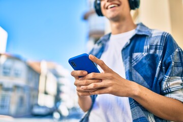 Young hispanic man smiling happy using smartphone and headphones at the city.