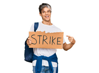 Young hispanic man holding strike banner cardboard smiling happy pointing with hand and finger