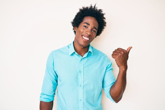 Handsome african american man with afro hair wearing casual clothes smiling with happy face looking and pointing to the side with thumb up.