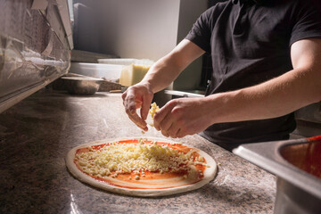 Cooking cheese pizza close up. Pizza base on the table. Male hands sprinkle cheese on the dough