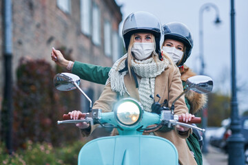 Fototapeta na wymiar Two women wearing masks and commuting on scooter