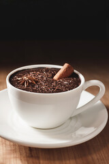 Hot chocolate drink in white cup with cinnamon stick and star anise on a wooden table with dark background