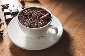 Hot chocolate drink in white cup, broken chocolate, cinnamon stick and star anise on a wooden table