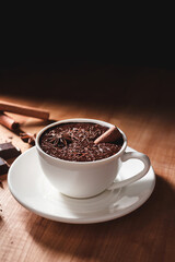 Hot chocolate drink in white cup, broken chocolate, cinnamon stick and star anise on a wooden table
