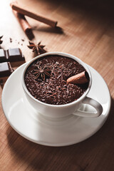 Hot chocolate drink in white cup, broken chocolate, cinnamon stick and star anise on a wooden table