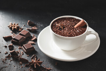 Hot chocolate drink in a white cup with cinnamon stick, broken chocolate cubes and star anise on...