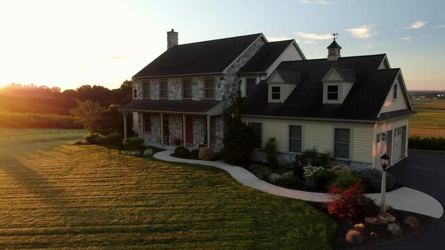 Large stone farm house during quiet morning sunrise in USA. Dramatic lighting on house and garage. Rise and shine summer scene. Aerial drone shot.