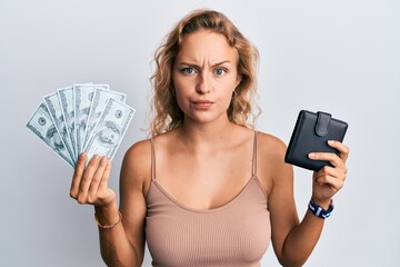 Beautiful caucasian woman holding wallet and dollars skeptic and nervous, frowning upset because of...